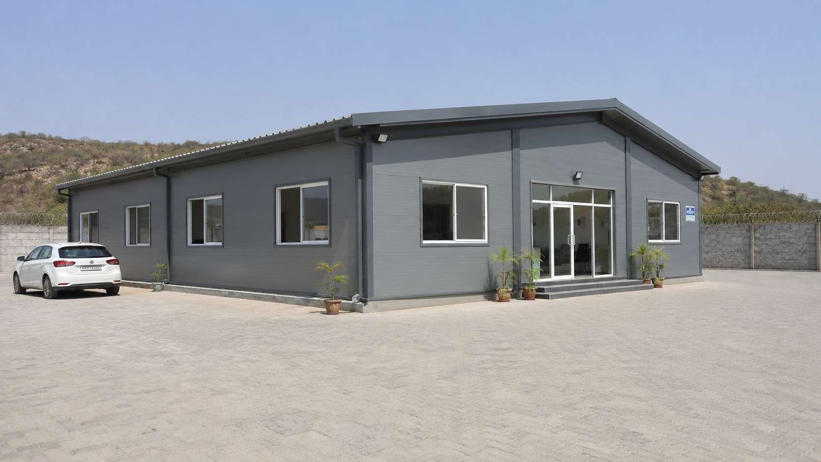 Steel grey steel prefab building with windows and glazed entry on a fenced business compound.