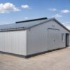 Grey steel prefab building with wide access doors and a paved approach in a working compound.