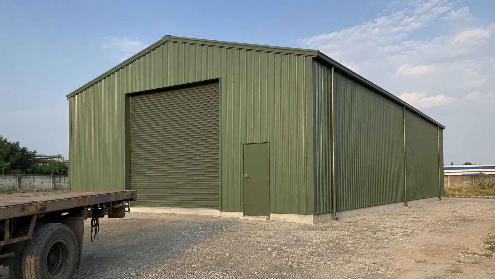 A sage-green 40×20 ft steel shed assembled on a prepared plot with a delivery truck nearby