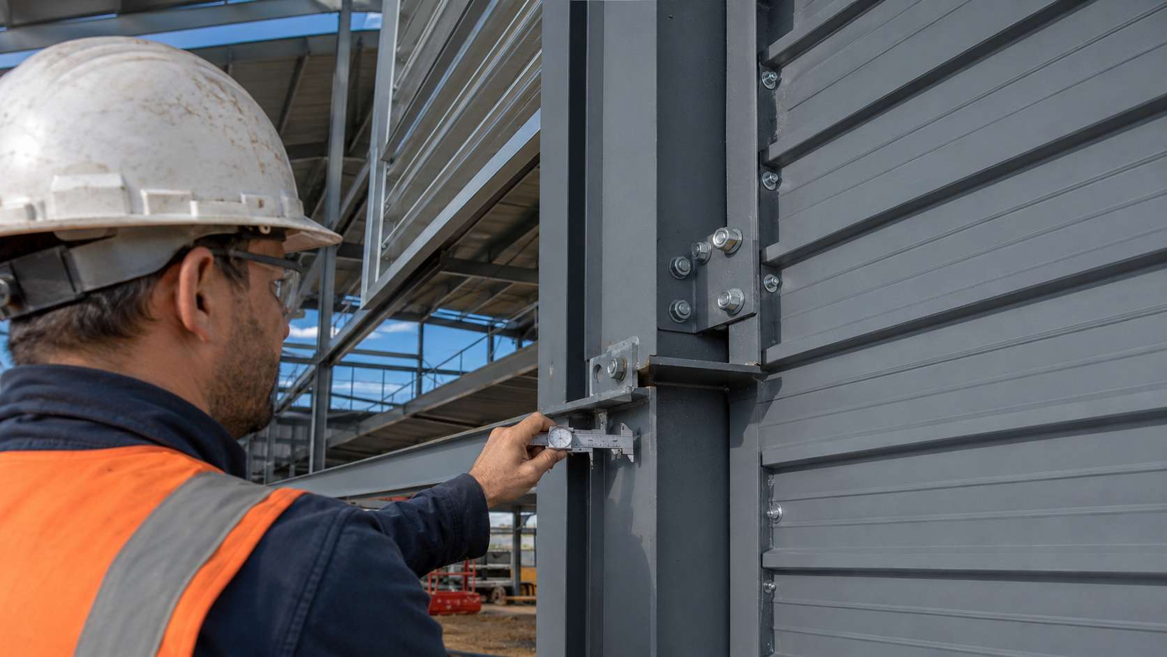 A worker inspecting the steel frame and grey cladding junction of a steel shed on site