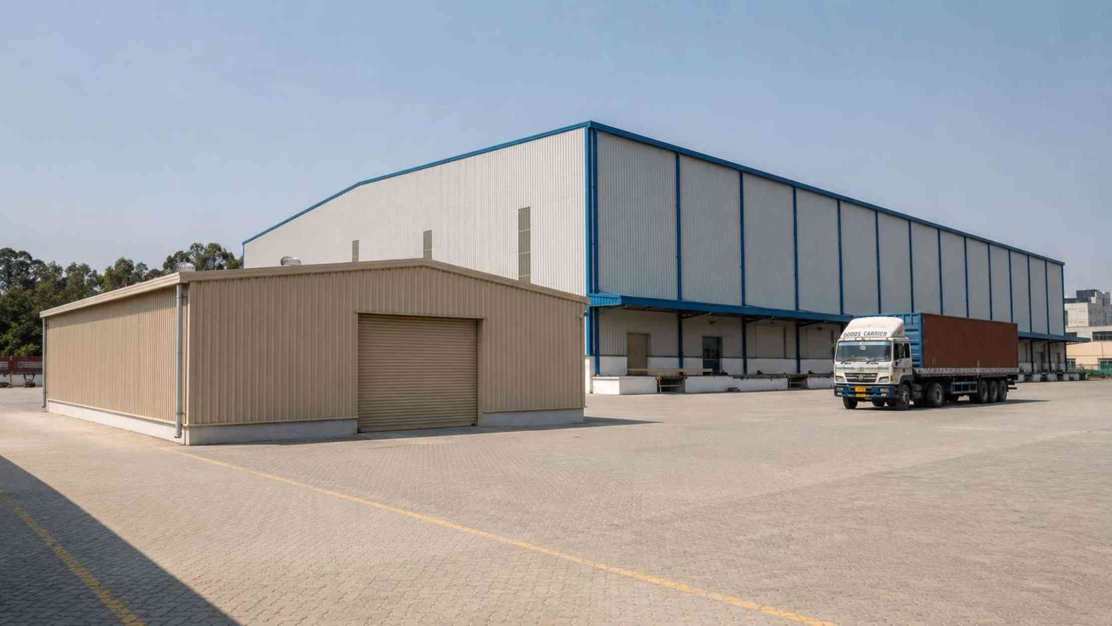 Beige storage shed in front of a much larger warehouse showing the size difference between the two.