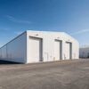 White three-bay storage shed showing its full length and roller-shutter loading doors.