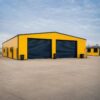 Yellow steel storage shed with two navy roller doors for loading goods and equipment.