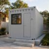 Front entry view of a pearl grey SAMAN tiny container home with single door and window on an Indian residential plot