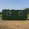 Side view of a green 20-ft tiny container home on levelling pads at a rural Indian residential plot