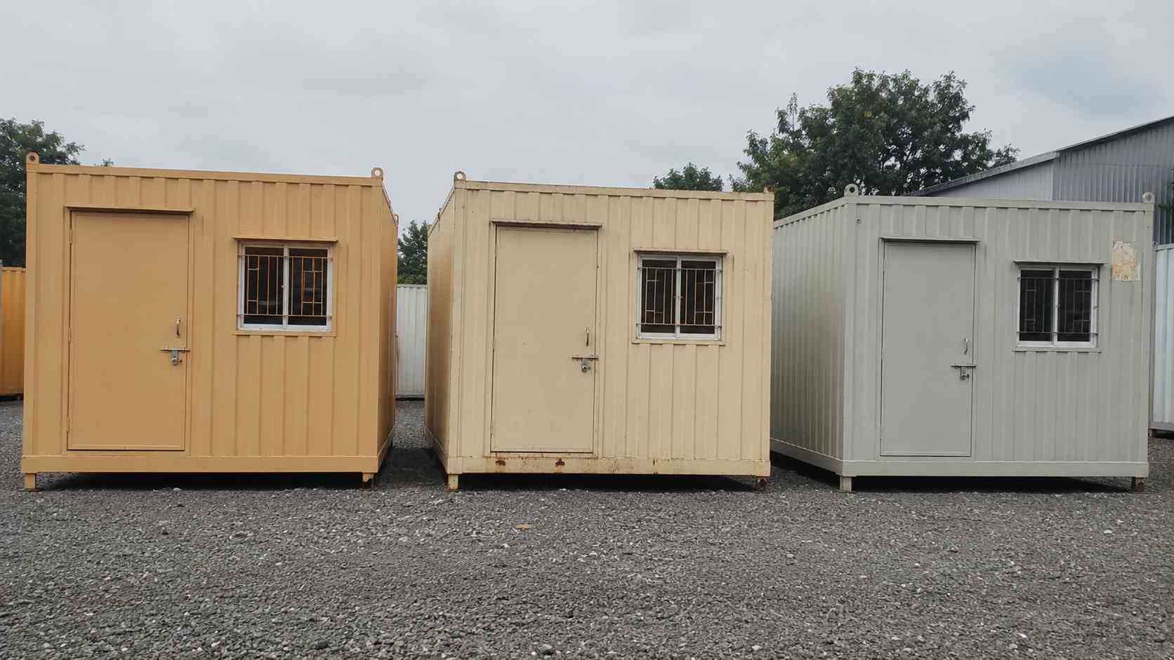Three portable cabins side by side at an Indian display yard — new beige cabin, weathered used cabin, and a rental unit.