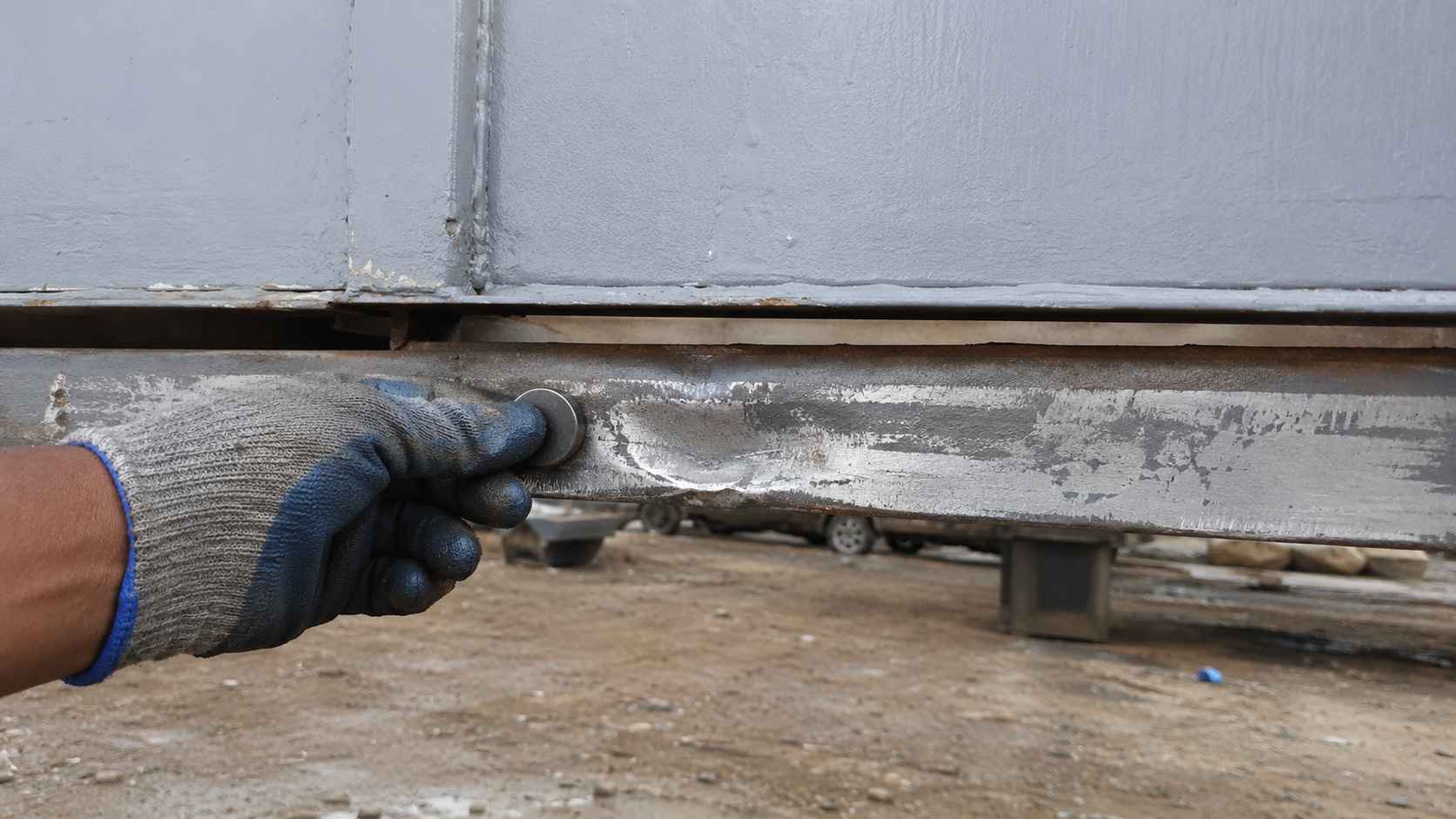 Close-up of a Steel Grey used porta cabin's base frame with a magnet test on the rust-ground channel.