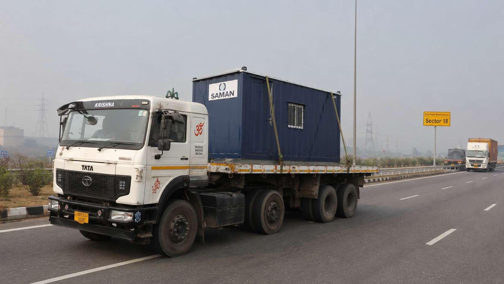  SAMAN porta cabin secured with Olive Drab ratchet straps on a heavy-goods truck en route from Jalpura to a Noida sector.