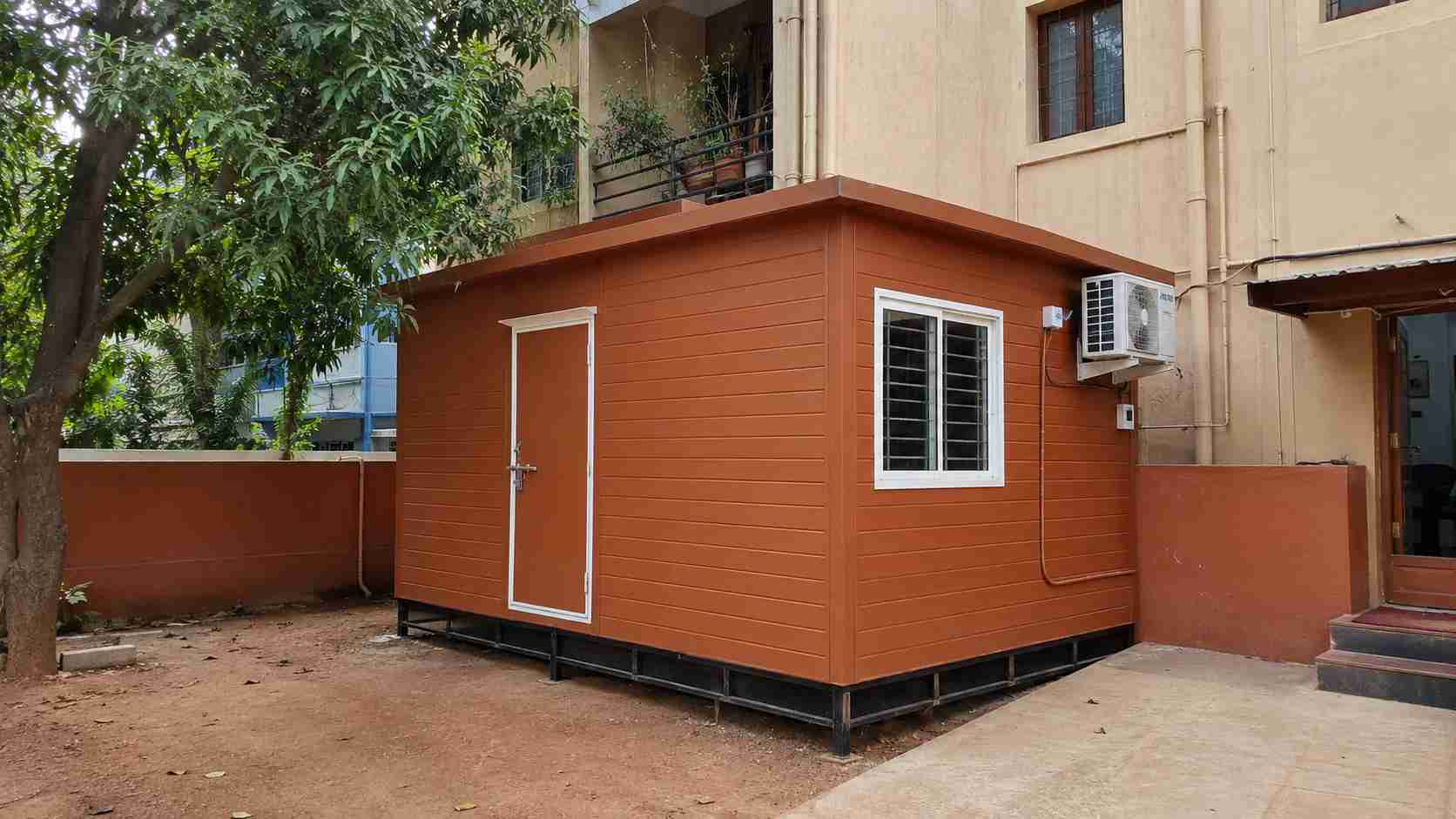 A brick terracotta 10×15 ft porta cabin installed as a small office on a Frazer Town private residential plot in Bangalore.