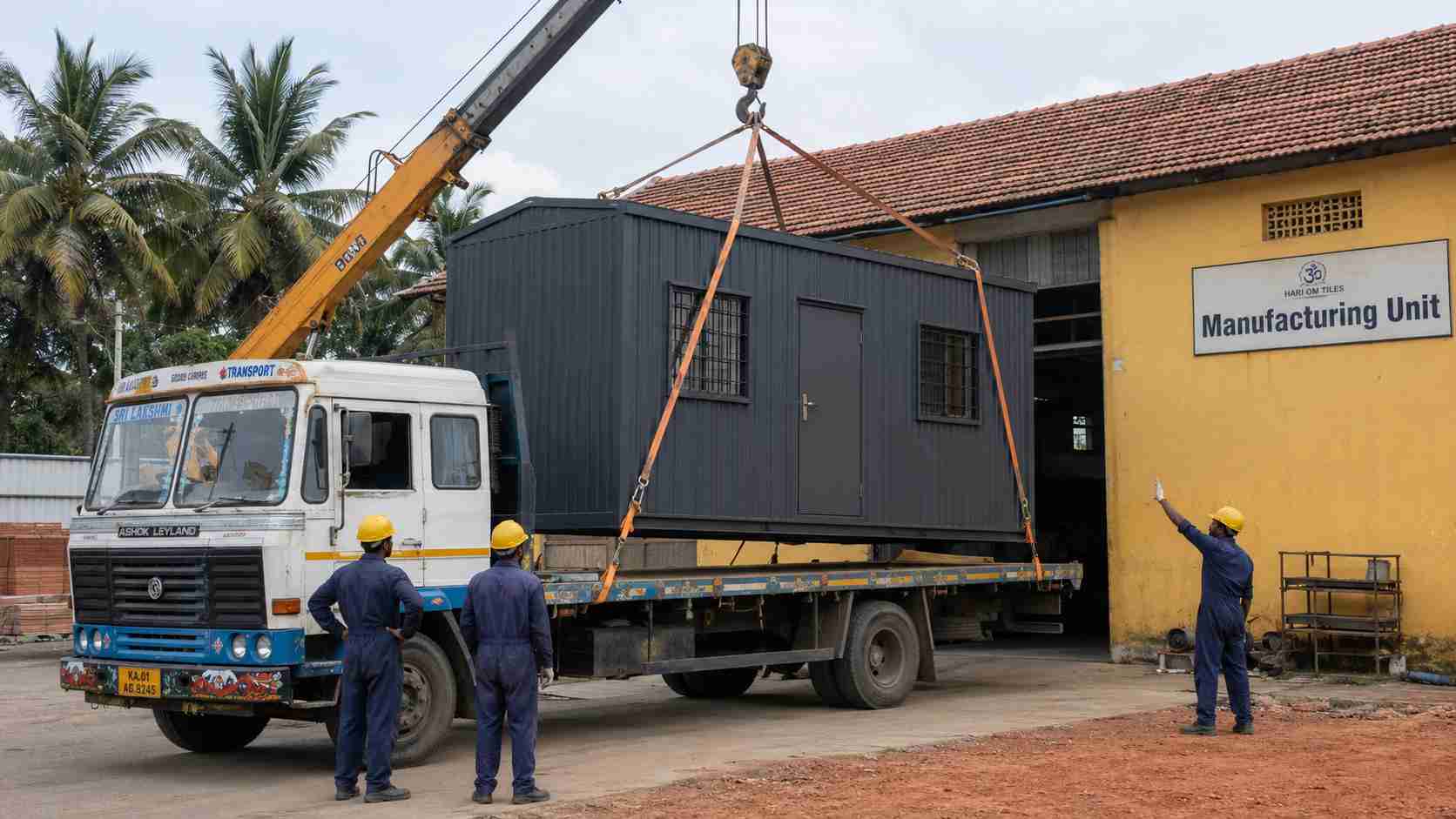 Slate charcoal porta cabin being loaded onto a flatbed truck at a manufacturing yard near Bangalore for site dispatch.