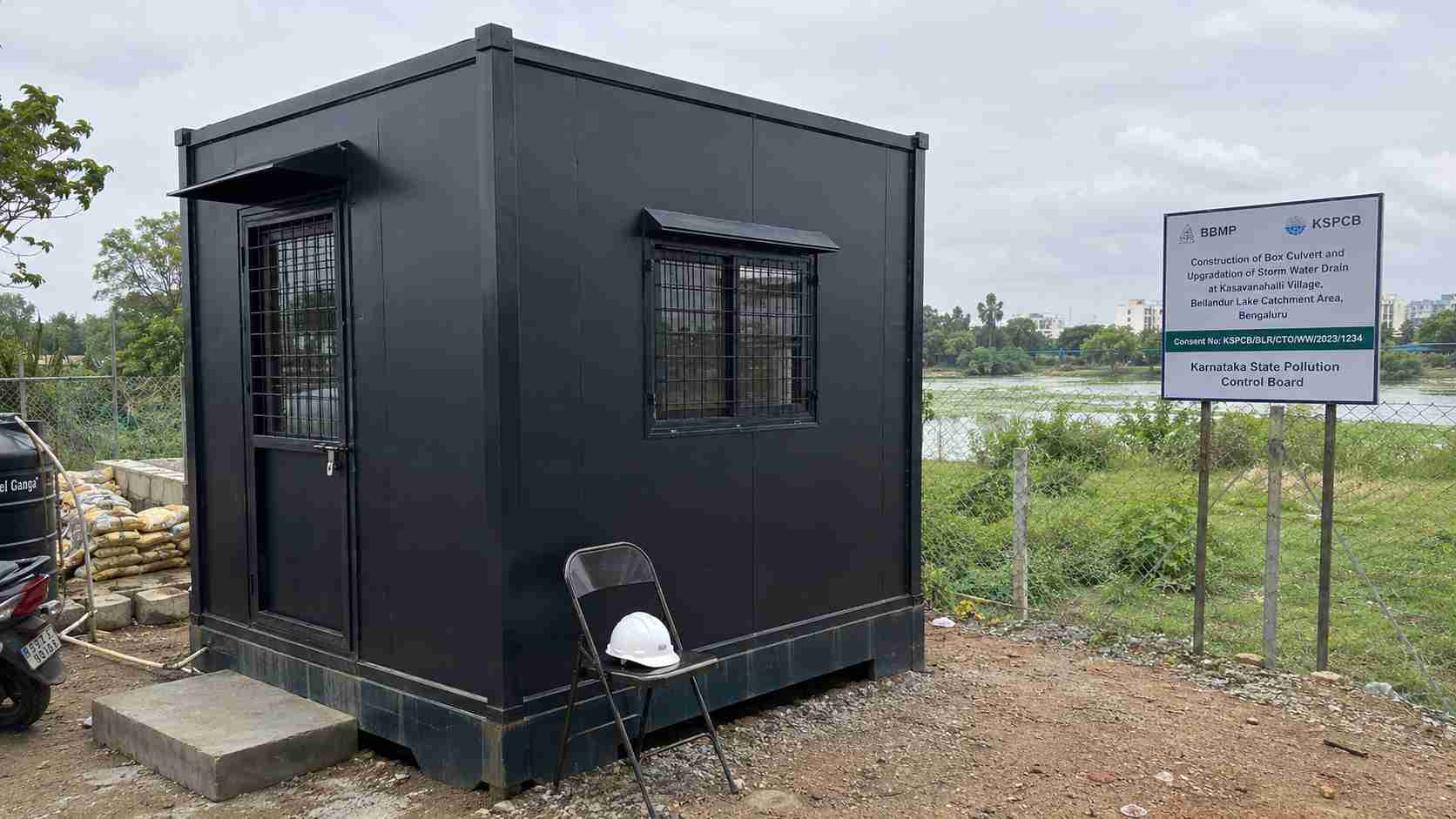 Graphite Black porta cabin used as a Bellandur Lake catchment civic-works site office near a BBMP cleanup zone.