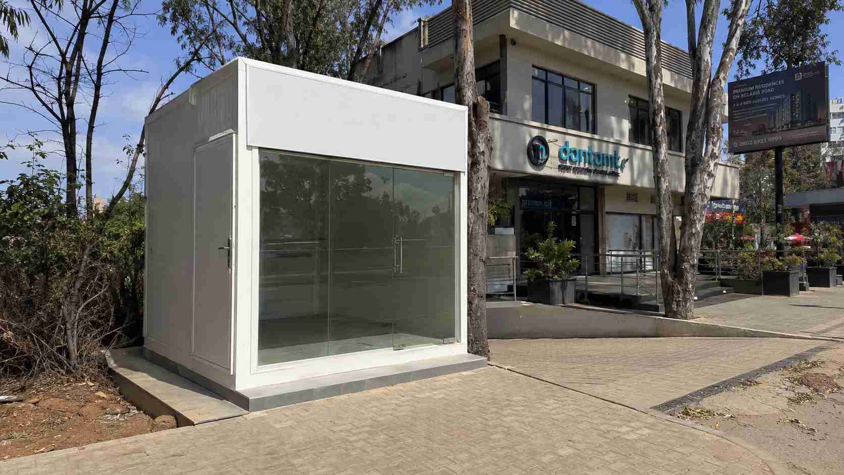 Pure-white shop-front porta cabin installed on a Bellary Road frontage plot in Hebbal — Profile B clinic or retail fitout.