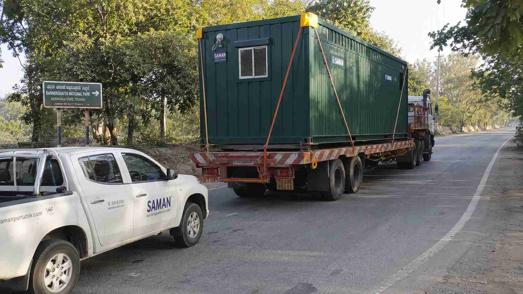 A Forest Green SAMAN porta cabin being delivered on a low-bed trailer along Anekal Road toward Bannerghatta village near the BNP gateway zone.