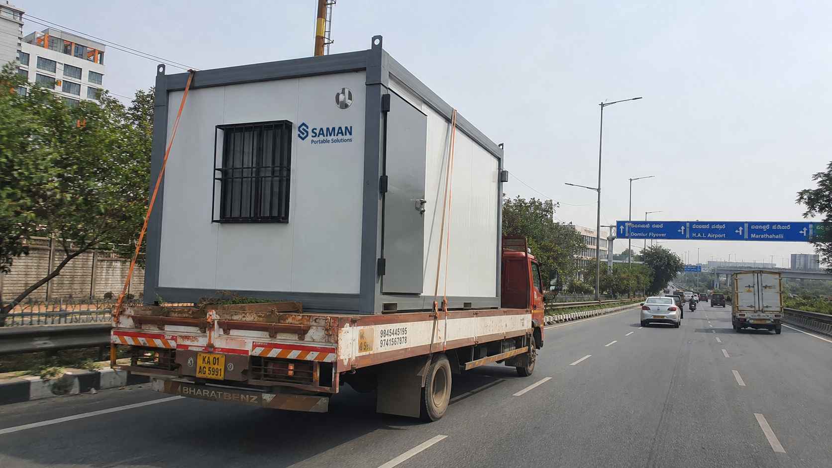 Steel Grey SAMAN porta cabin on a flatbed truck on Outer Ring Road approaching Domlur from Gopasandra factory, Bangalore.