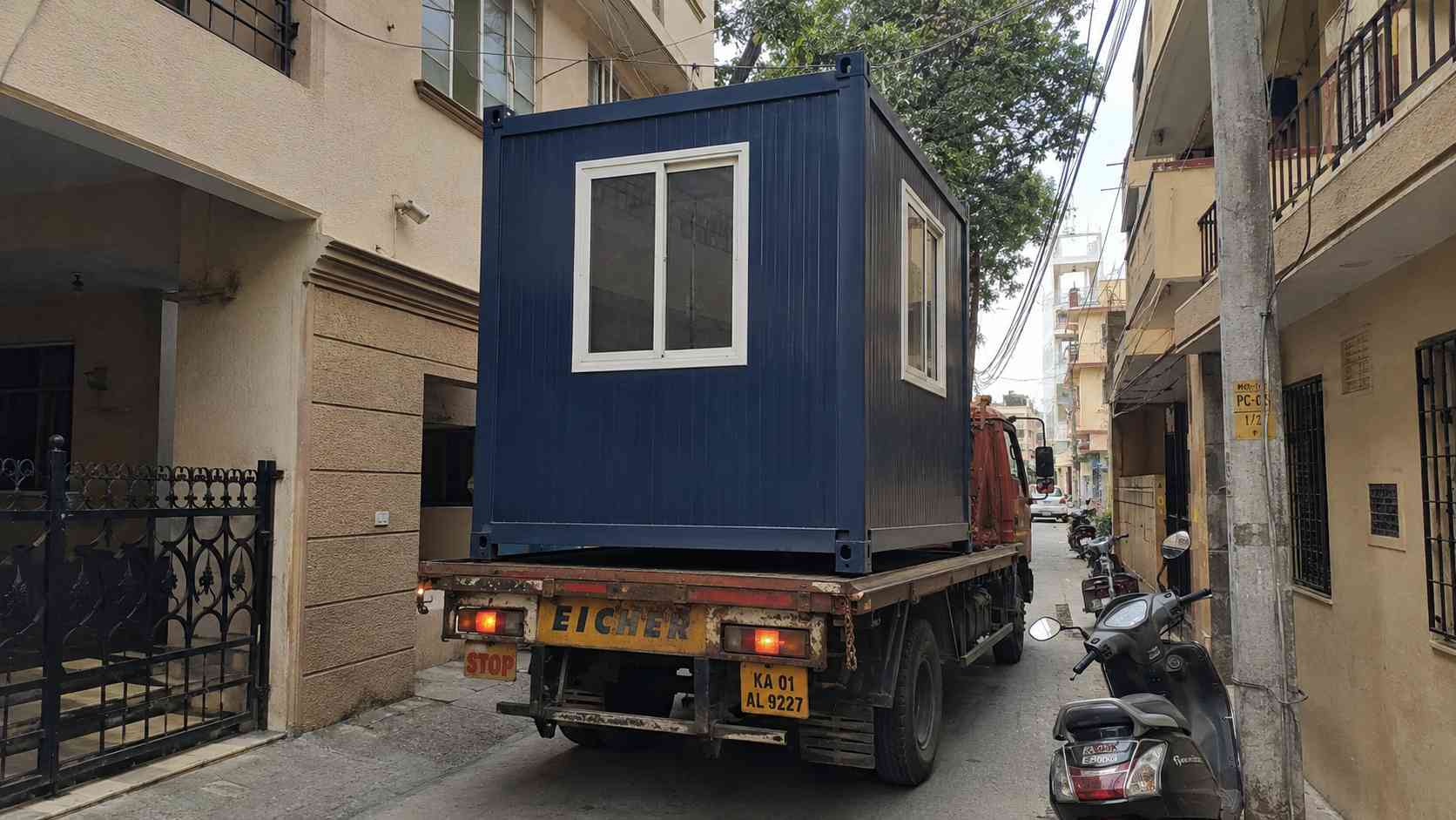  A navy blue 10×10 ft porta cabin being delivered on a flatbed truck through a narrow inner-Frazer Town lane in Bangalore.
