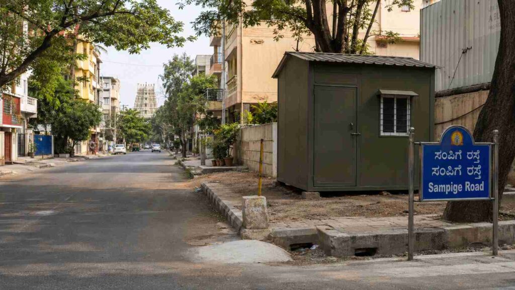 Olive Drab porta cabin on a Malleshwaram formal-grid road in Northwest Bangalore, near heritage-residential buildings and education belt.