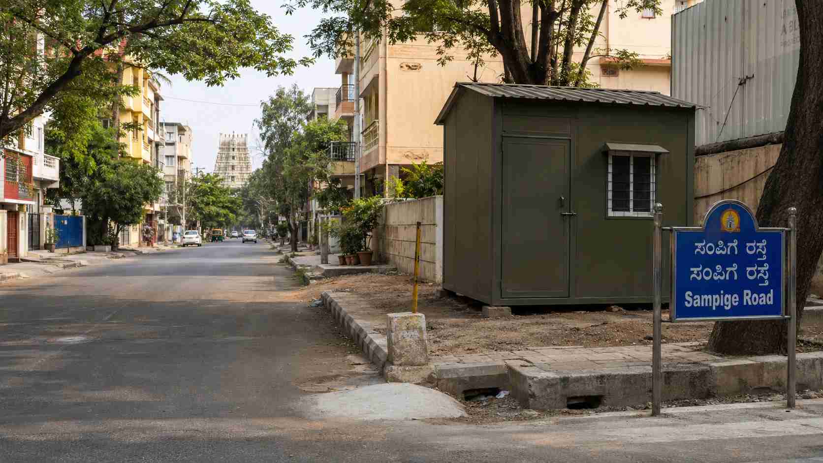 Olive Drab porta cabin on a Malleshwaram formal-grid road in Northwest Bangalore, near heritage-residential buildings and education belt.