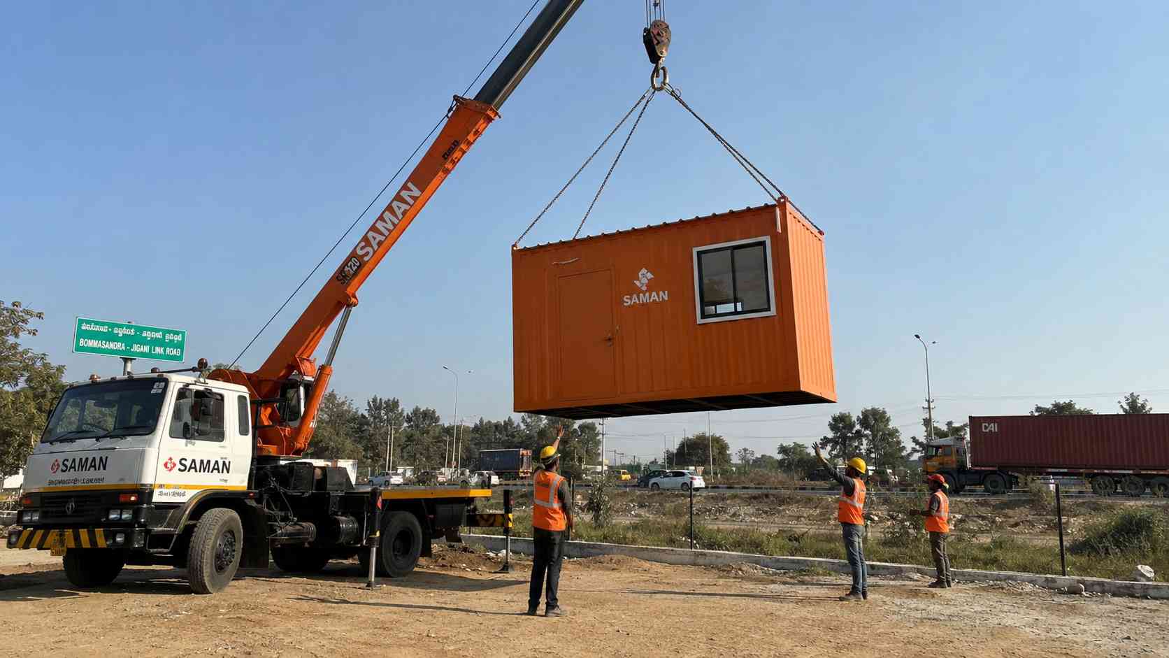 Safety Orange SAMAN porta cabin being craned onto a Jigani Industrial Area plot from a Gopasandra dispatch truck