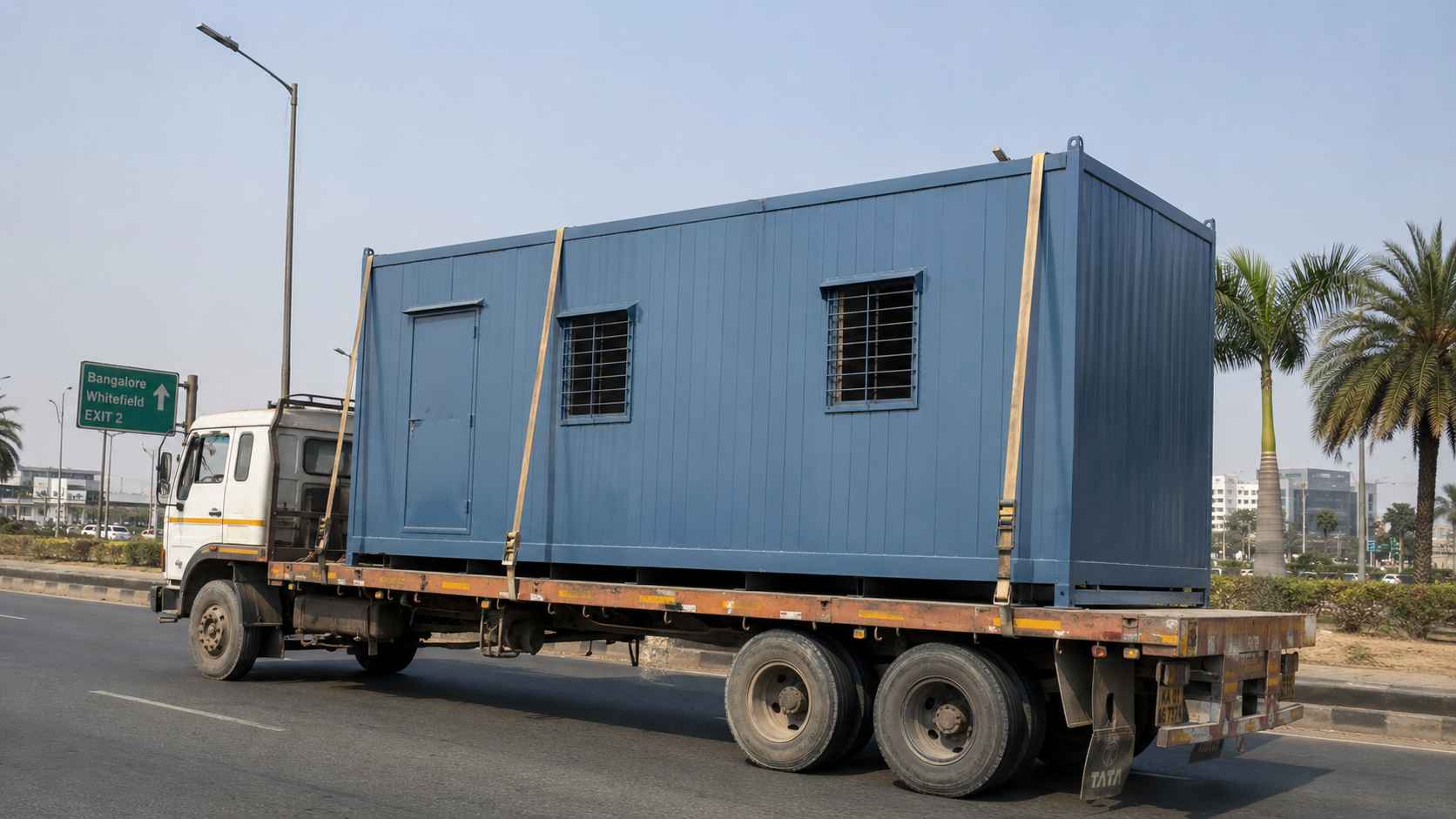 Steel Blue porta cabin loaded single-piece on a flatbed truck approaching Whitefield via Bangalore ORR.