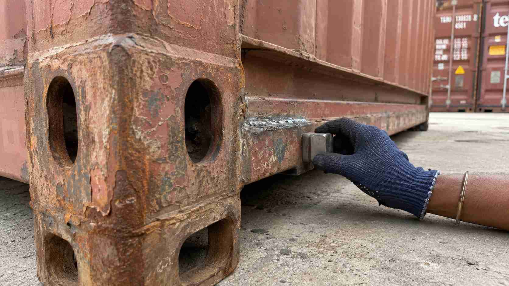  Close-up of a rusted ISO corner casting on a used shipping container being magnet-tested during inspection.