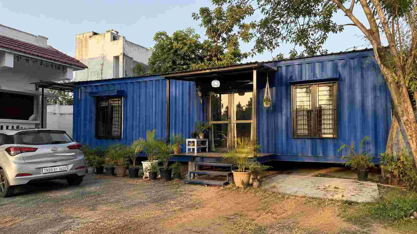 Royal cobalt blue SAMAN container house on a family plot with a porch and entry steps.