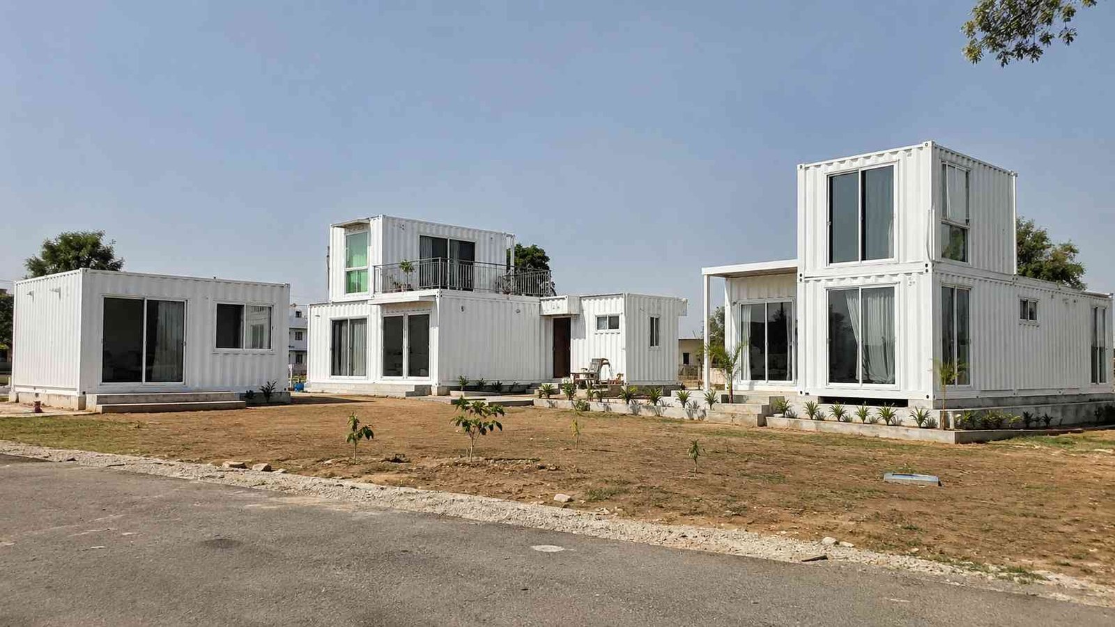 Row of finished SAMAN container houses in pure white on a cleared residential plot in India.