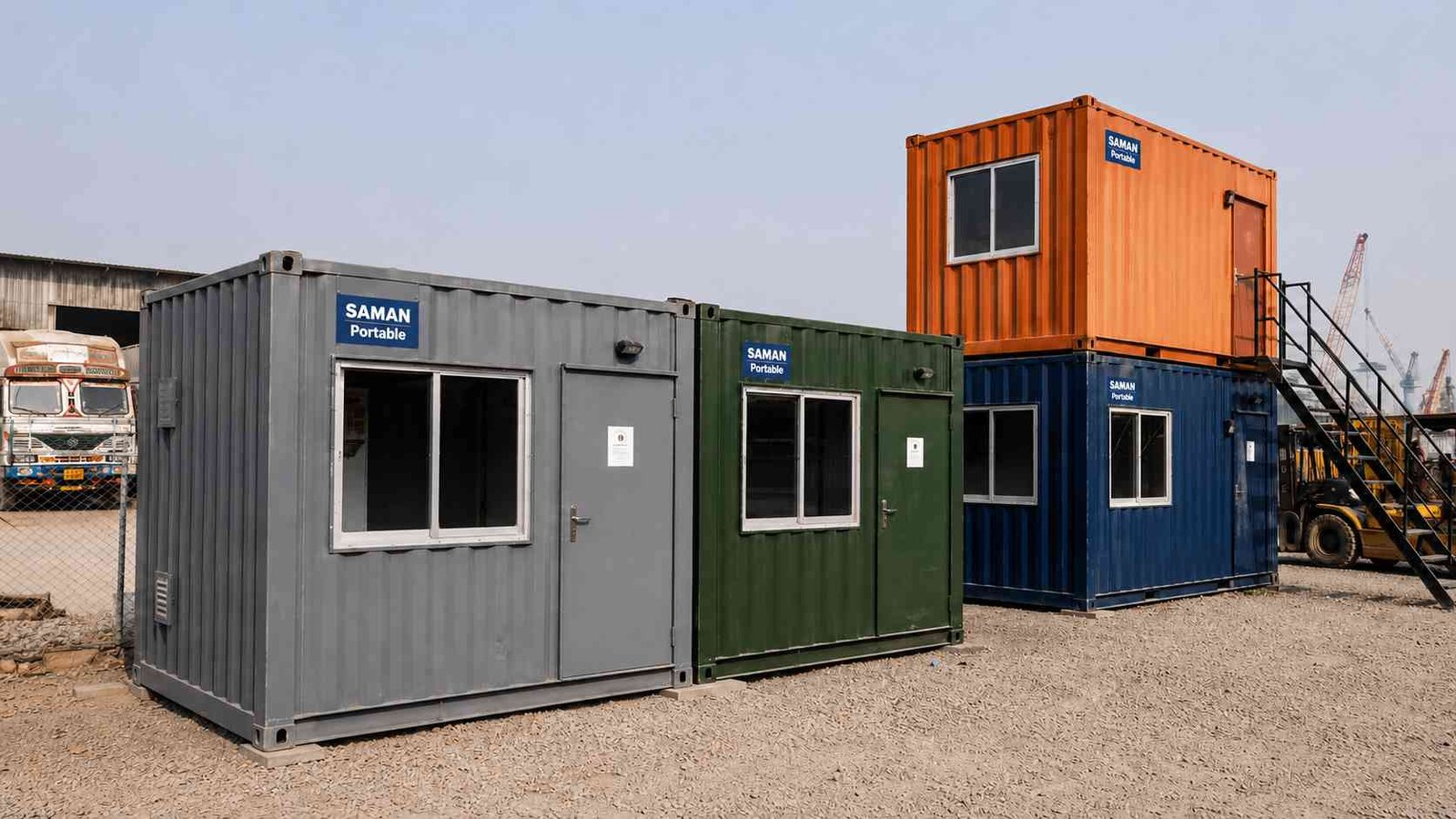 Steel grey, forest green and navy ISO-grade container offices lined up at an Indian industrial compound.

