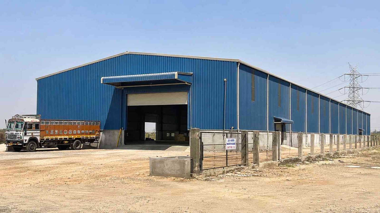 Steel-blue industrial shed with clear-span frame on an Indian industrial plot, roller shutter open.