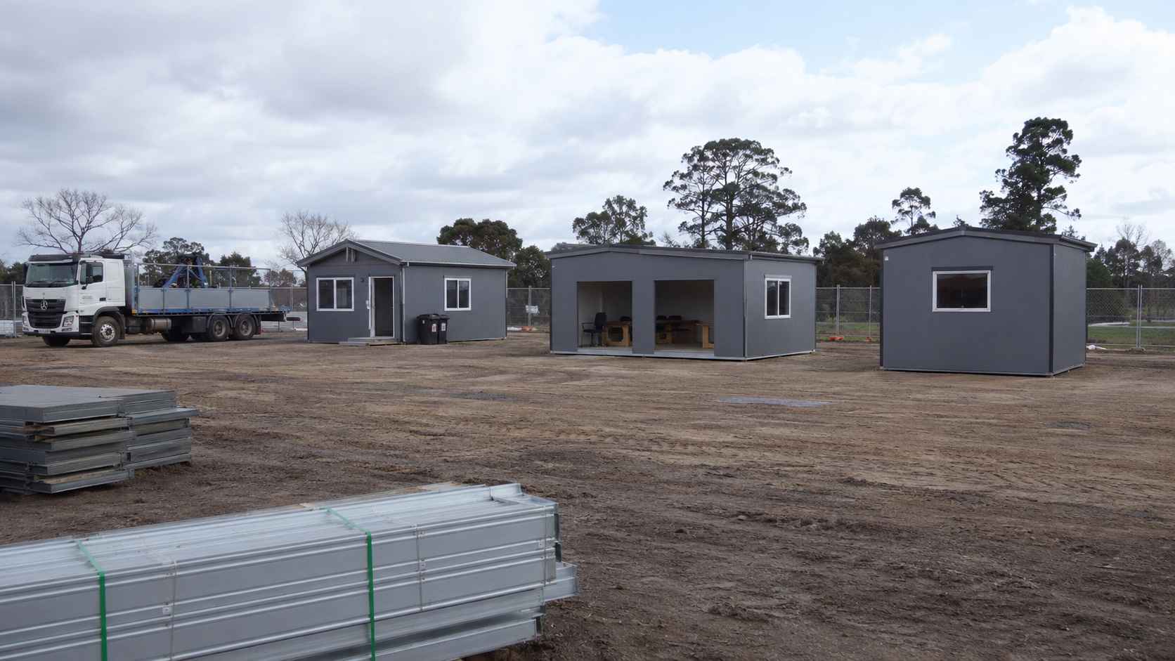 Steel-grey prefab labor cottage and shed units on a bare early-stage construction site