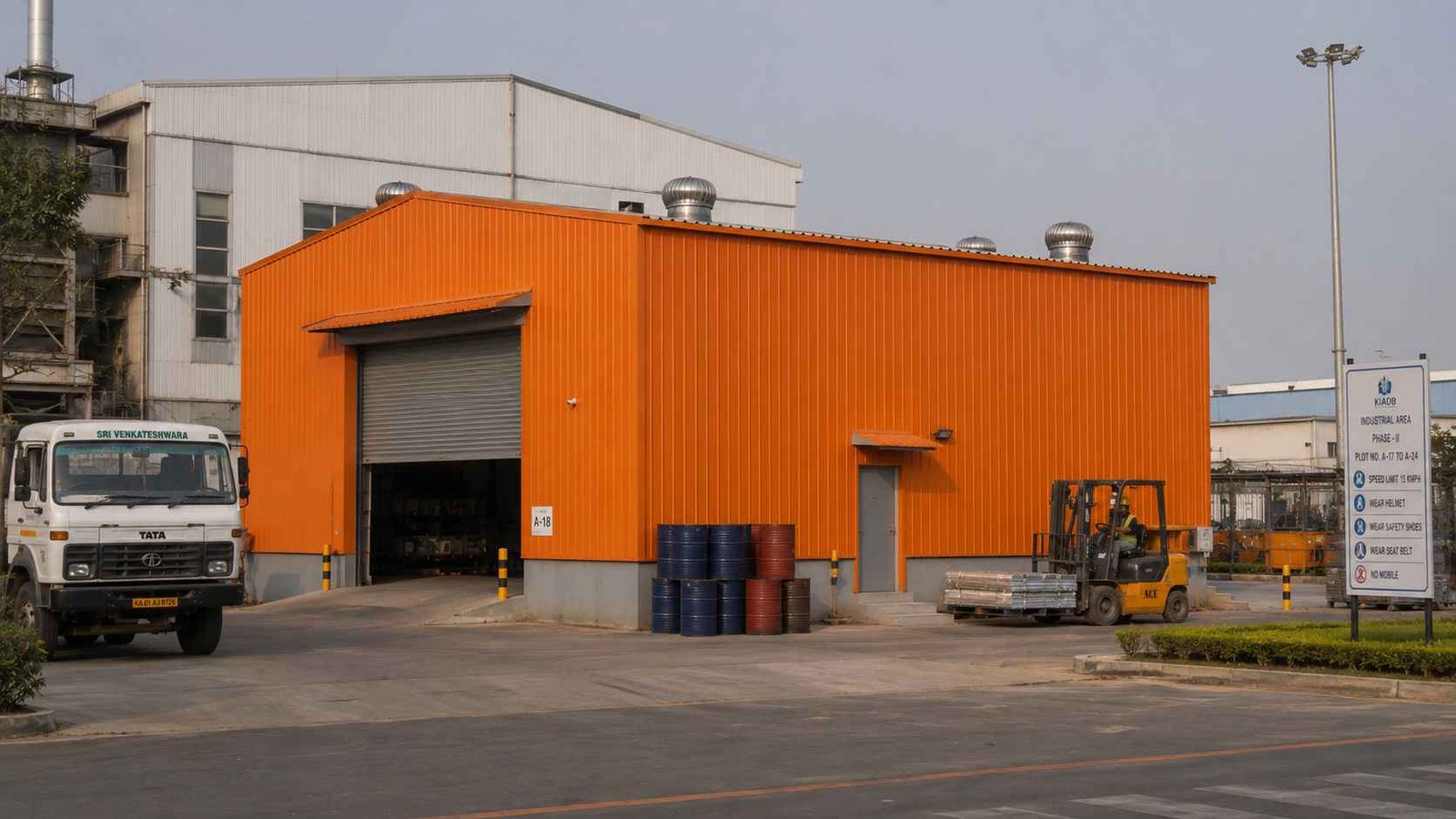 Safety orange prefab industrial building with roller shutter at an Indian factory site with industrial truck and forklift.