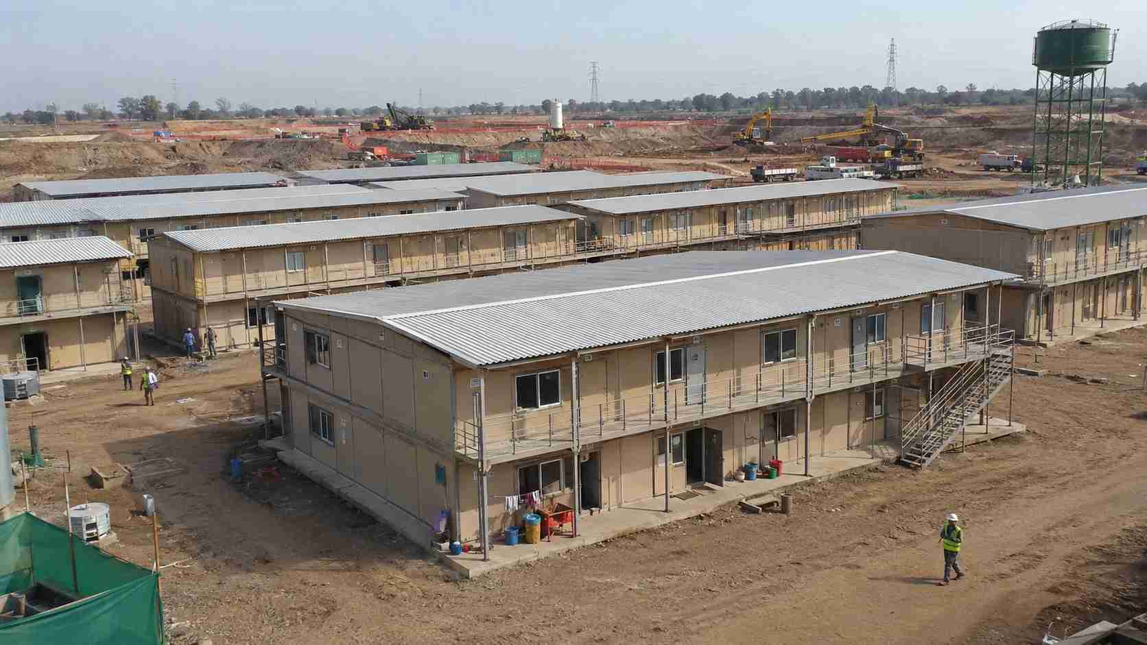 Sandstone-beige multi-block prefab labor camp with a two-storey G+1 unit on a large project site.