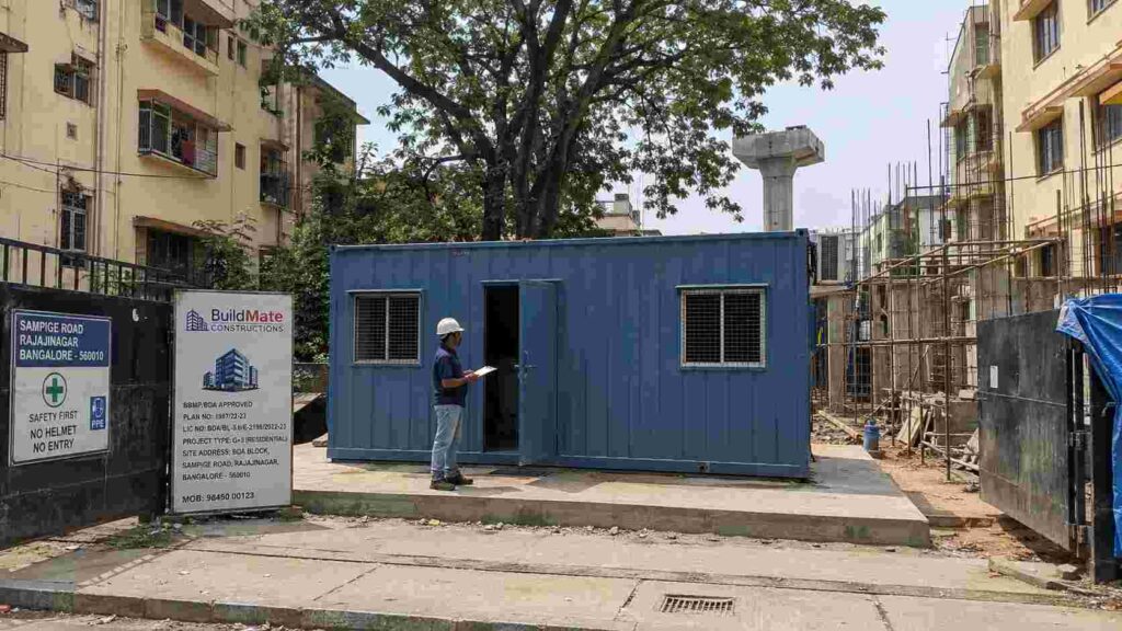 Steel Blue MS porta cabin installed at a BBMP/BDA-approved G+3 residential redevelopment site on Sampige Road, Rajajinagar, Bengaluru 560010, with a site supervisor inspecting the unit.