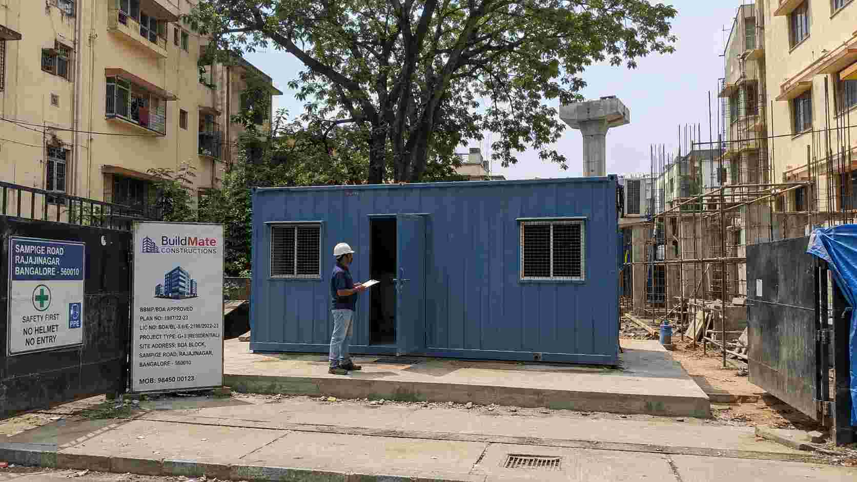 Steel Blue MS porta cabin installed at a BBMP/BDA-approved G+3 residential redevelopment site on Sampige Road, Rajajinagar, Bengaluru 560010, with a site supervisor inspecting the unit.